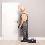 Young handyman installing a white door with an electric hand drill in a room