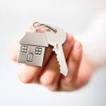 Holding house keys on house shaped keychain concept for buying a new home